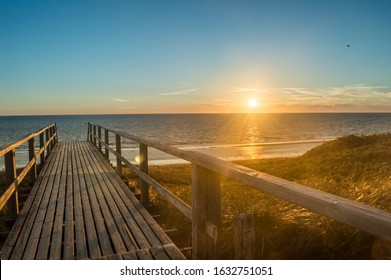 beautiful view onto the North Sea from a boardwalk on sylt taken at sunset with dunes in the foreground, the beach in the background and the warm light of the evening sun coloring the whole picture  - Powered by Shutterstock