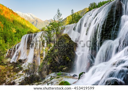 Beautiful view of the Pearl Shoals Waterfall among scenic wooded mountains and evergreen forest in Jiuzhaigou nature reserve (Jiuzhai Valley National Park), China. Amazing autumn landscape at sunset.