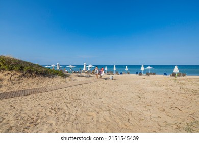 Beautiful View Of People Walking To Mediterranean Beach With Sun Loungers And Umbrellas. Greece. Europa. 08.25.2021.