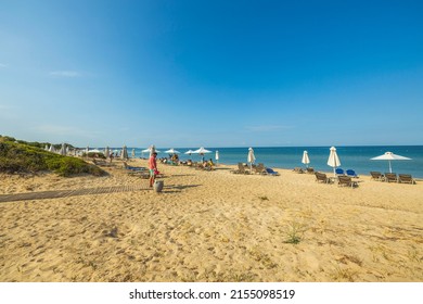 Beautiful View Of People Walking On Mediterranean Beach With Sunny Sun Loungers And Umbrellas. Greece. Nea Potidea. 08.25.2021.