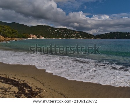 Beautiful view of sand beach Plage du Layet at the rocky mediterranean coast near town Le Lavandou at the French Riviera, France on sunny day in autumn season with hills covered by green forest.
