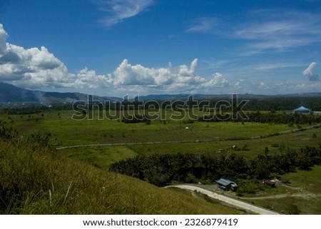The beautiful view of the Sentani valley during the day can be seen from a height with a stretch of green mountains and blue sky with white clouds.