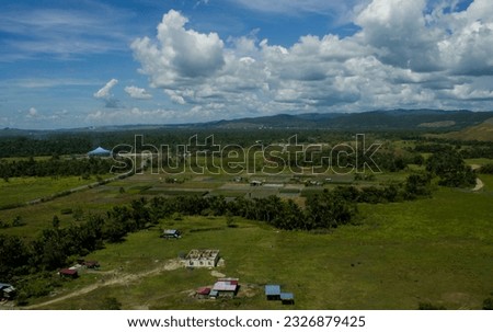 The beautiful view of the Sentani valley during the day can be seen from a height with a stretch of green mountains and blue sky with white clouds.