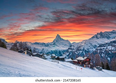 Beautiful View Of Snow Covered Houses In Village. Majestic Mountain Range Against Cloudy Sky During Sunset. Holiday Homes In Alpine Region During Winter.