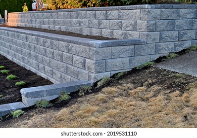 A Beautiful View Of A Stone Retaining Wall Build In Two Tiers Along A Slope In The Front Yard In Grey Color.