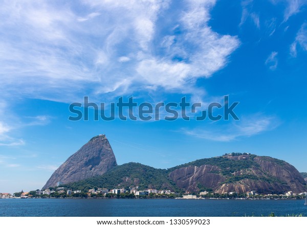 Beautiful view of the Sugar Loaf mountain in Rio\
de Janeiro, Brazil, on a beautiful and relaxing sunny day with blue\
sky and white clouds