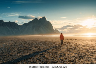 Beautiful view of sunrise over Vestrahorn mountain with a tourist man walking on black sand beach in summer at Stokksnes peninsula, Iceland