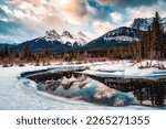 Beautiful view of Three Sisters Mountains with snow covered on bow river reflection in the morning on winter at Canmore, Alberta, Canada