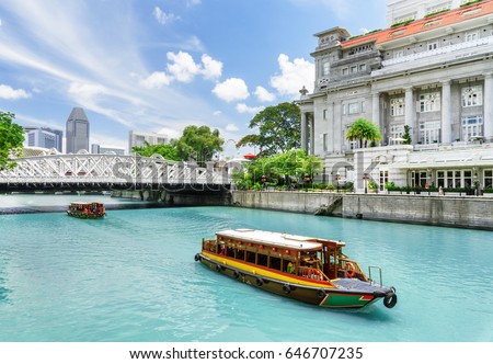 Beautiful view of traditional tourist boats sailing along the Singapore River with azure water in downtown of Singapore. Scenic summer cityscape. Singapore is a popular tourist destination of Asia.
