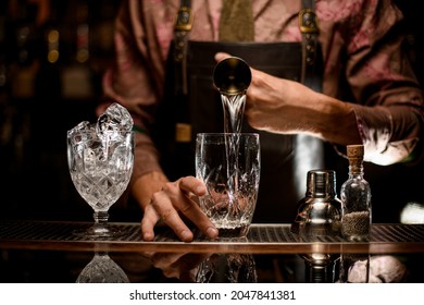 beautiful view of transparent glasses on bar counter in one of which the hand of man bartender accurate pours drink from jigger