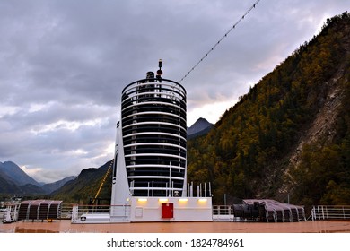 A Beautiful View Of Upper Deck Of Cruise Ship With Smoke Stack Surrounded By Mountains And Storm Clouds