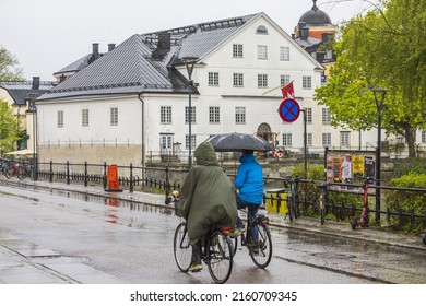 Beautiful view of Uppsala city center with people cycling along river embankment during heavy rain. Sweden. Uppsala. 05.14.2022.