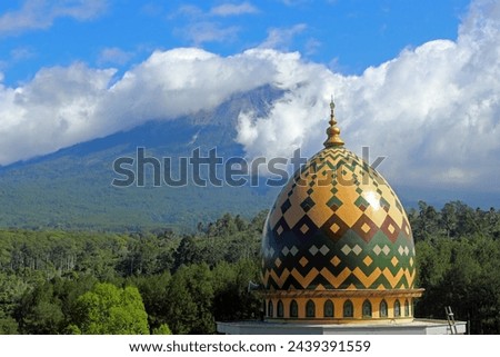 Beautiful view of a village with a mosque dome in the foreground and cloudy Mount Semeru in the background. Thematic images for Ramadan and Eid.