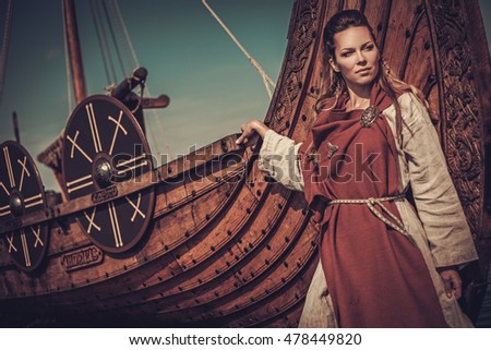 Beautiful viking woman standing near Drakkar on the seashore.