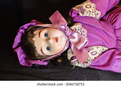 A Beautiful Vintage Doll In Purple Prairie Style Dress And Hat On Black Background