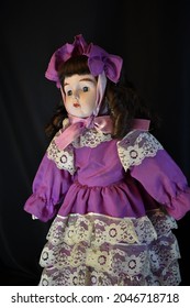 A Beautiful Vintage Doll In Purple Prairie Style Dress And Hat On Black Background