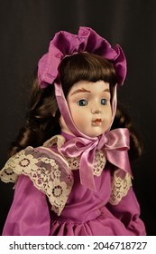 A Beautiful Vintage Doll In Purple Prairie Style Dress And Hat On Black Background