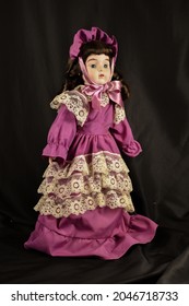 A Beautiful Vintage Doll In Purple Prairie Style Dress And Hat On Black Background