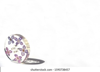 Beautiful violet button isolated on white background situated bottom left. Lilac flower in epoxy resin, suitable for text insert.