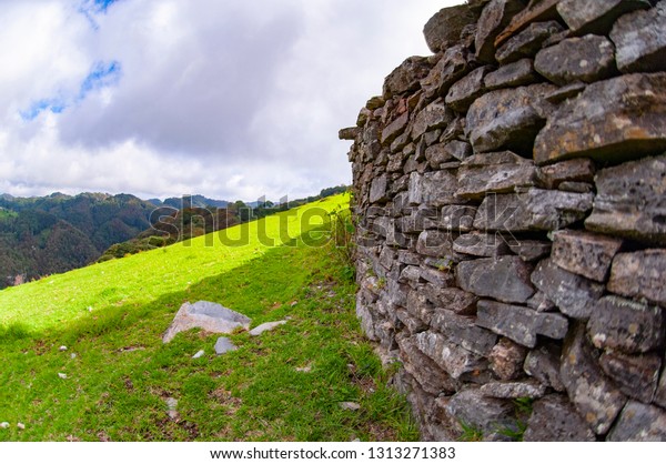 beautiful wall made of small flat planks that\
divide a dirt road and a beautiful field of grass surrounded by\
mountains