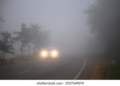 A beautiful wallpaper of a car traveling on the foggy forest road in Shimoga or Shivamogga,Karnataka, India with its headlights or headlamps on. Low visibility due to thick fog.