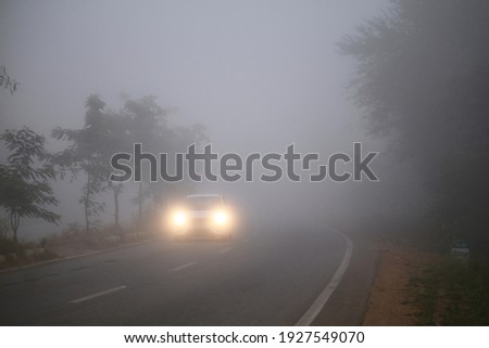 A beautiful wallpaper of a car traveling on the foggy forest road in Shimoga or Shivamogga,Karnataka, India with its headlights or headlamps on. Low visibility due to thick fog.