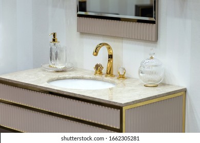 A beautiful washbasin with a gold tap and fittings. Marble sink, round led mirror, gold dispenser.