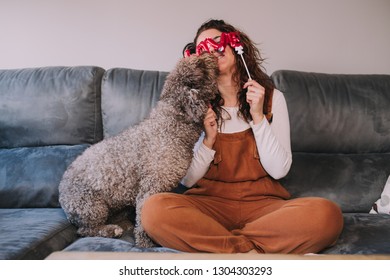 A beautiful water dog is giving kisses to her owner's face. Her owner is puting  a balloon with the word love over the eyes of pet.