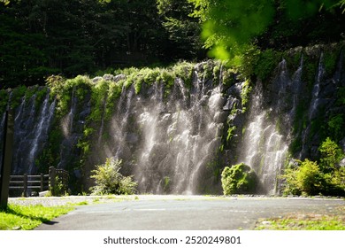 A beautiful waterfall cascading down a rocky cliff surrounded by lush green foliage. - Powered by Shutterstock