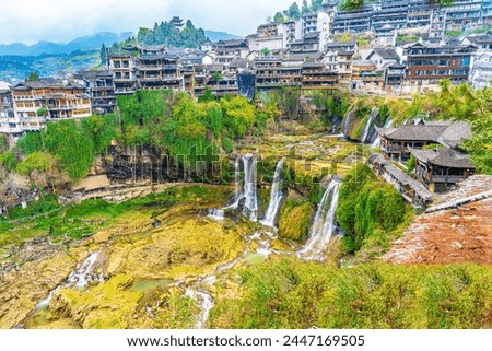 Beautiful waterfall in Furong Zhen town with traditional Chinese style  buildings on the top in a blur background of mountain, temple, and fields from afar and a blur foreground of hay roof