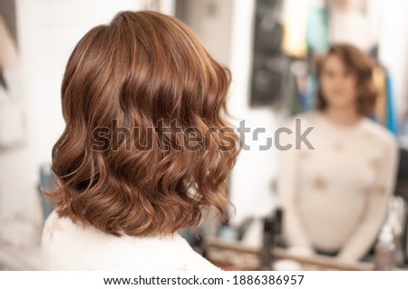 Beautiful wavy hair styling on a young woman with medium brown hair indoors, view from the back with reflection in the mirror, close-up