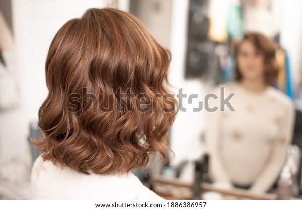 Beautiful wavy hair styling on a young woman\
with medium brown hair indoors, view from the back with reflection\
in the mirror,\
close-up
