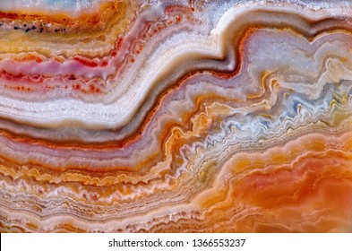 Beautiful wavy texture of natural stone Perelivt or Ural agate. Agate-perelivt from Urals, Russia. Beautiful red white brown colorful layered structure and pattern of quartz aggregate stone