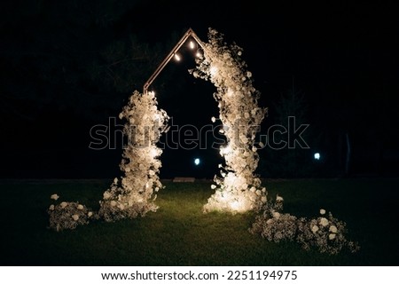 beautiful wedding arch with white flowers and lamps in the garden, night ceremony