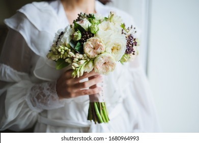 Beautiful wedding bouquet in bride's hands, wedding underwear, details. The girl in a white dress holding a bouquet of white, pink flowers and greenery, decorated with silk ribbon