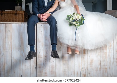 Beautiful wedding couple sitting on wooden pier, swung their legs and enjoying wedding.