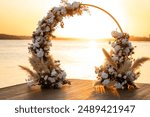 Beautiful wedding decoration at sunset. Wedding ceremony venue. Round arch, white chairs, cute, fashionable decor. Part of holiday decor, flower arrangement.