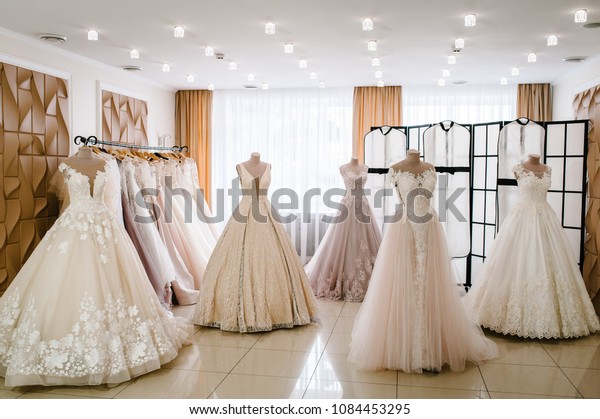 Beautiful wedding dresses, bridal\
dress hanging on hangers and mannequins in studio, shop. Fashion\
look. Interior of bridal salon. Wedding show room trendy,\
modern.