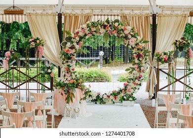 Beautiful wedding set up. Area of the wedding ceremony. Round arch, white chairs decorated with flowers, greenery. Cute, trendy rustic decor. Part of the festive decor, floral arrangement.