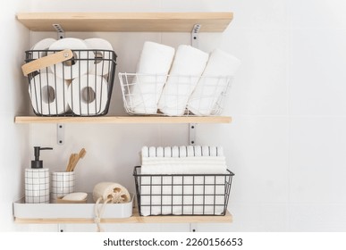 Beautiful white bathroom. Wooden shelves. Rolled towels, stacked towels and baskets. Soap, washcloth, toilet paper and toothbrushes. Indoor flowers. Eco style, minimalism.