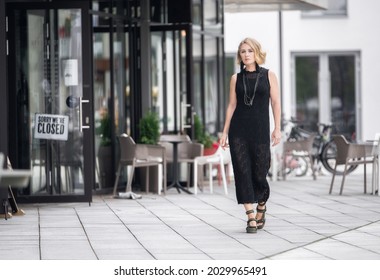 Beautiful White Caucasian Woman Is Walking On Sidewalk In Vilnius, Lithuania. Local Cafe Shops In Background. No People Around.