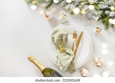 Beautiful white Christmas table setting with golden balls, bottle of champagne and napkin ring as deer on white background. View from above. Copy space. Xmas festive dinner.