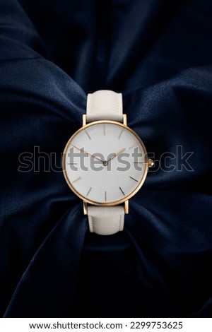 Beautiful white gold women's watch on a beautiful blue fabric background. The concept of a fashionable women's white luxury watch with a white dial and a golden case on a beautiful background.
