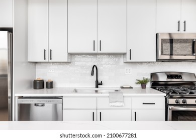 A beautiful white kitchen detail shot with a tiled backsplash, white cabinets, stainless steel appliances, and black hardware and faucet. - Powered by Shutterstock