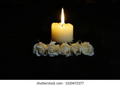 Beautiful White roses with a burning candle on the dark background. Funeral flower and candle on table against black background with copy space. Funeral symbol. Mood and Condolence card concept