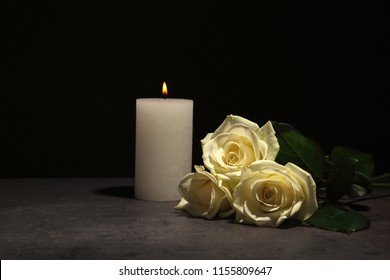 Beautiful White Roses And Candle On Table Against Black Background. Funeral Symbol