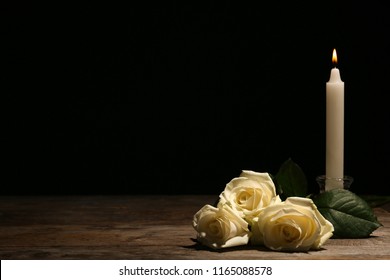 Beautiful White Roses And Candle On Table Against Black Background. Funeral Symbol