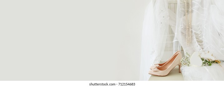 Beautiful white wedding dress, shoes, gold diamond tiara and veil on chair.