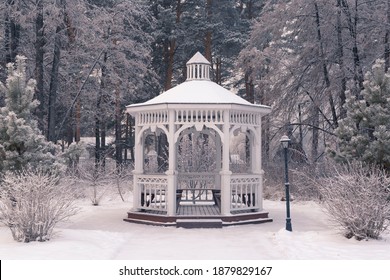 Beautiful white wooden gazebo in a winter park against the backdrop of snowy trees. Park within the city.  - Powered by Shutterstock