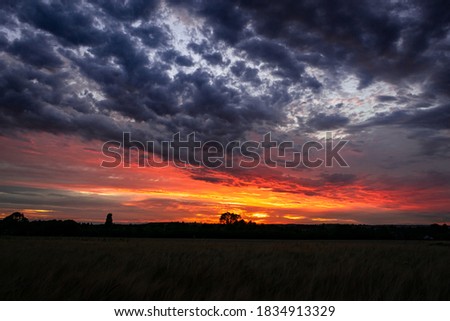 Beautiful wide angle view for dark and dramatic sunset sky with clouds, astonishing sun set in bright colors on British agricultural grounds, most amazing view in UK, high contrast and saturation 